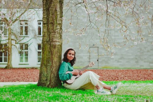 een vrouw die met haar rug tegen een boom aan zit en ukelele zit te spelen